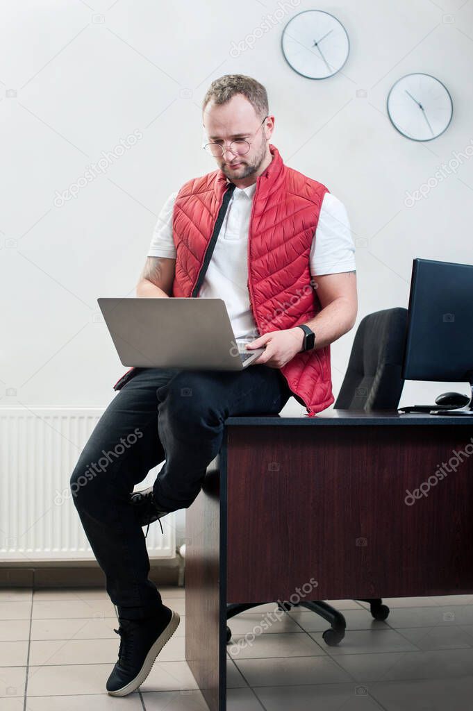 young man in a red sleeveless shirtworking with laptop in office