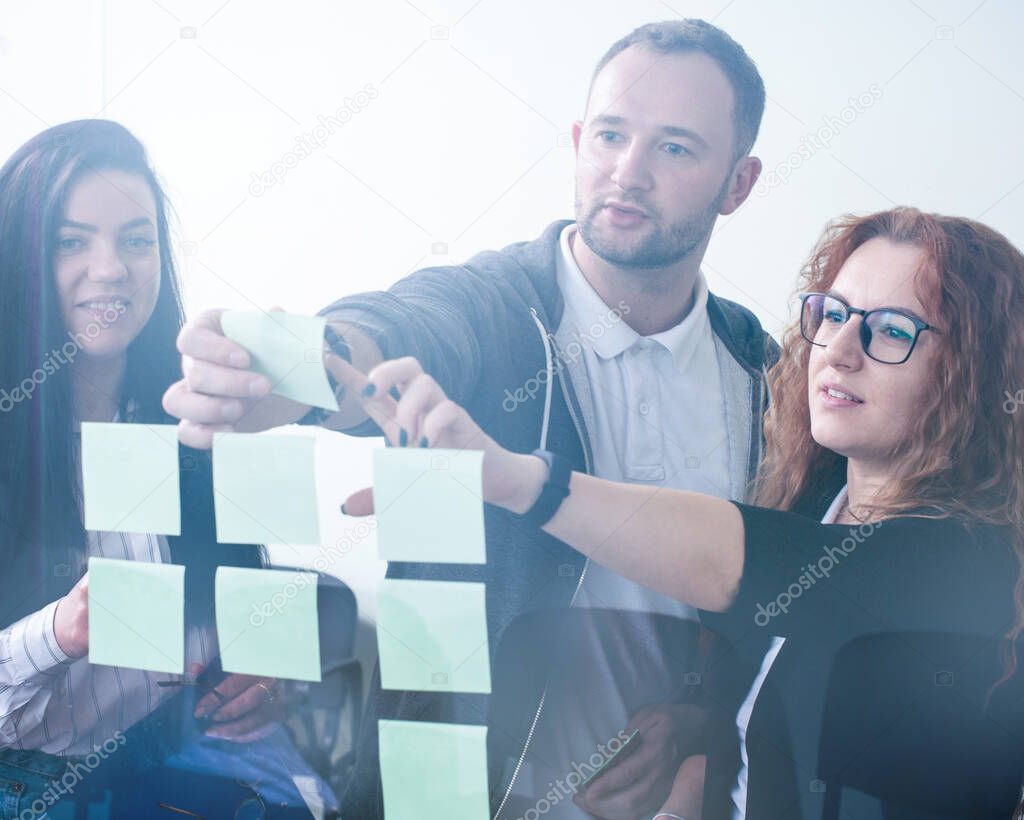 Office team work, people discussing in front of glass wall using post it notes and stickers at startup