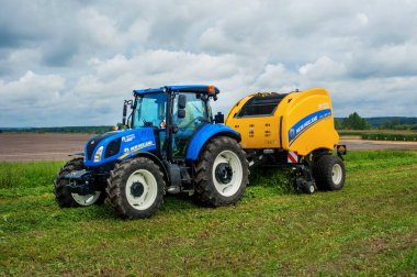Bilohir 'ya, Khmelnytsky bölgesi, Ukrayna - 15 Ağustos 2019: Tarım teknolojisinin sunumu - New Holland, yeni mavi traktör T5.110S ile Baler Roll kemeri 180 ile tarım sergisi FARM Day' de tanıtım alanında hareket halinde.
