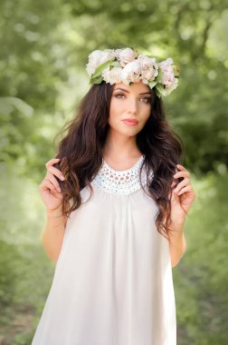 Bahar çelengi ve elinde şakayık demeti olan beyaz elbiseli genç bayan.