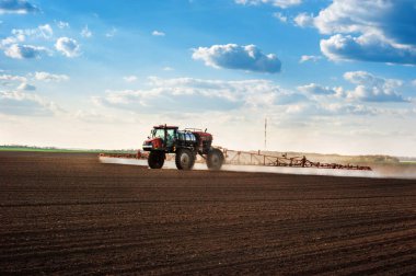 Tarlada uzun kolları olan büyük püskürtücü ilkbahar manzarasında bulutlu gübre yapar.