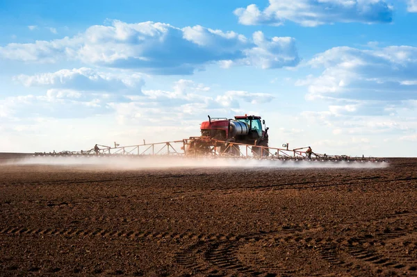 self-propelled sprayer with long arms disperses fertilizers on agricultural fields, rear view, backlit jet