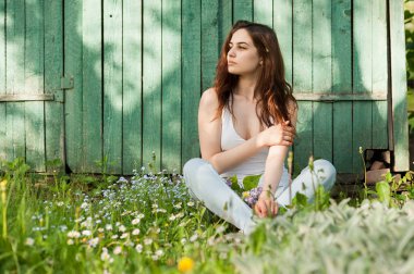 Çiçekler arasında bahar bahçesinde oturan genç kız, arka planda eski tahtalar, ışıklar ve gölgeler