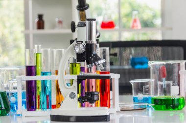 Laboratuvarda kırmızı, turuncu, mavi kimyasallar bulunan mikroskoplar ve ameliyat masasına yerleştirilen tüp.
