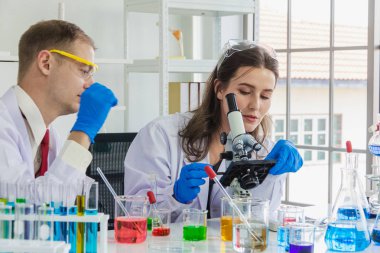 Beyaz kadın, mikroskopla erkek bilim adamının baktığı beyaz şişede laboratuvar ve sıvı kimyasallar konusunda danışmanlık yapıyor.