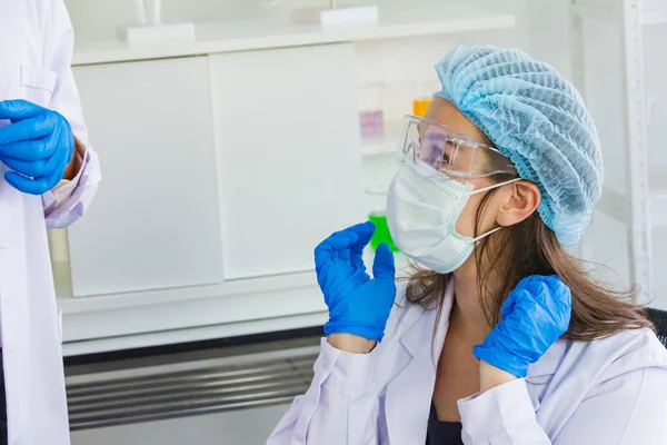 female scientist wearing safety glasses,dark blue glove,hairnet wearing mask,sitting in the laboratory