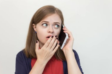 Genç beyaz kadın cep telefonuyla konuşuyor, korkmuş, şok olmuş, endişeli ya da üzgün görünüyor.