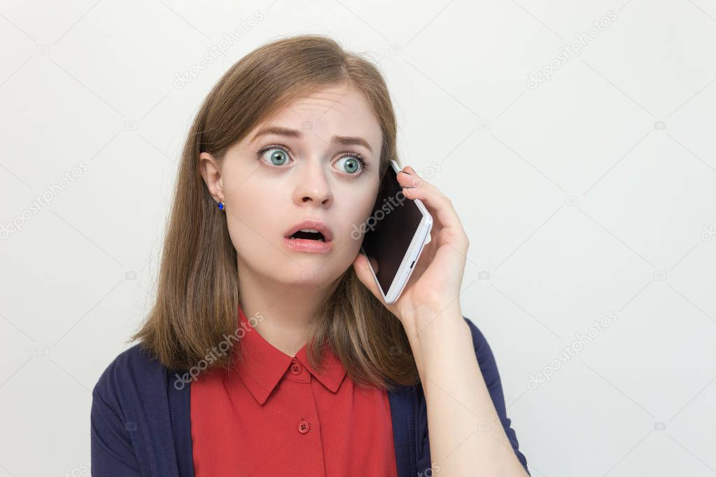 Young caucasian girl woman is talking on the mobile phone, looks scared, shocked, worried or sad