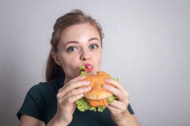 Gülümseyen beyaz kadın elinde tavuk burger tutuyor.