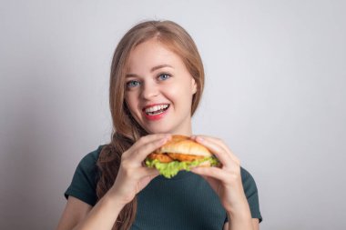 Gülümseyen beyaz kadın elinde tavuk burger tutuyor.