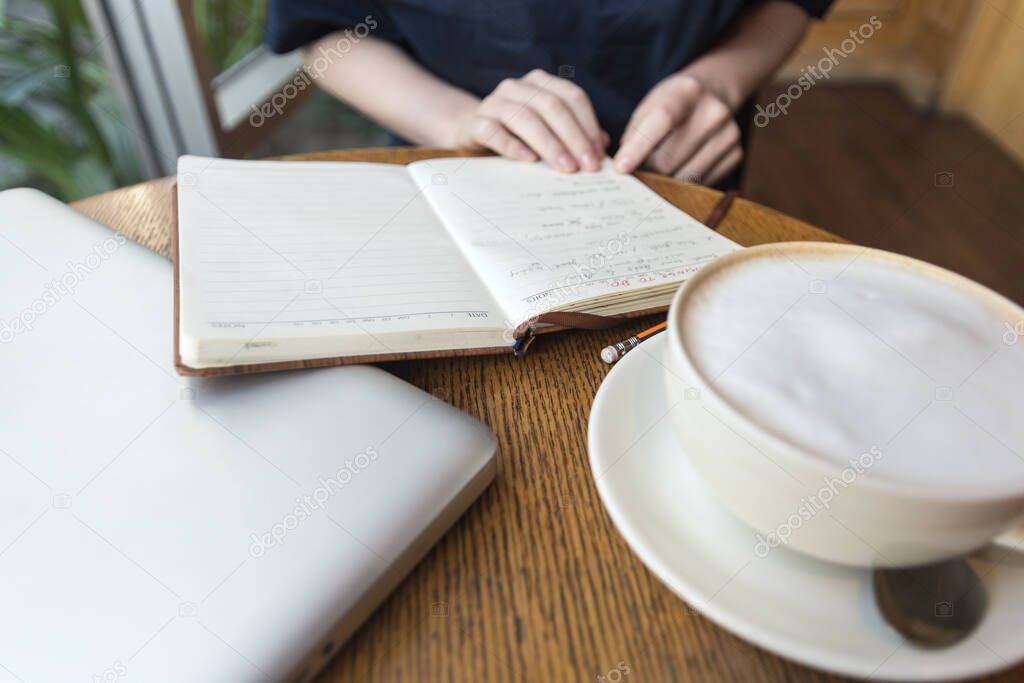 Woman's hands with coffee cup, laptop and notebook taking notes for business on table, close up