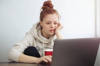 Genç beyaz kadın evde dizüstü bilgisayarın önünde sıkılmış görünüyor. Ev kavramından çalış
