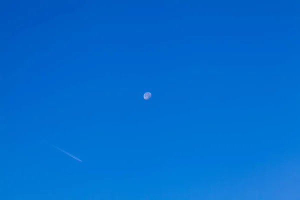 Blue sky with moon and trace from plane