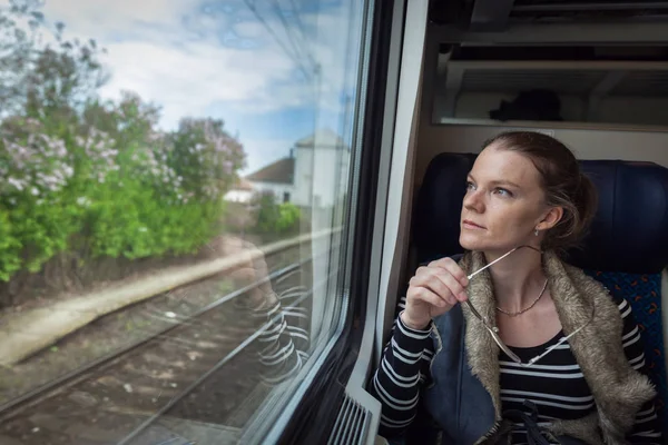 La joven está en el tren y mira a través de la ventana o — Foto de Stock