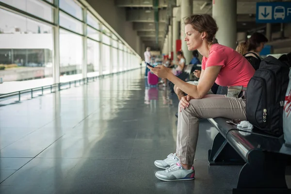 Giovane donna con cellulare in attesa di un autobus alla stazione — Foto Stock