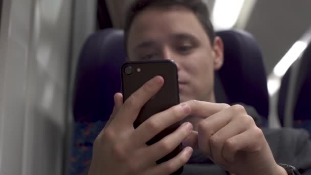 Jongeman die in een trein werkt en plezier heeft met een smartphone en muziek serveert — Stockvideo