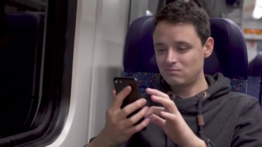 Genç adam trende çalışıyor, akıllı telefonuyla eğleniyor ve müzik sunuyor.