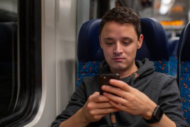 Trendeki genç adam akıllı telefonundan haberleri okuyor.