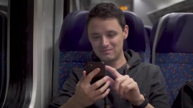 Genç adam trende çalışıyor, akıllı telefonuyla eğleniyor ve müzik sunuyor.