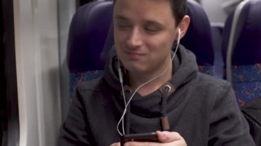 Genç adam trende çalışıyor, akıllı telefonuyla eğleniyor ve müzik sunuyor.