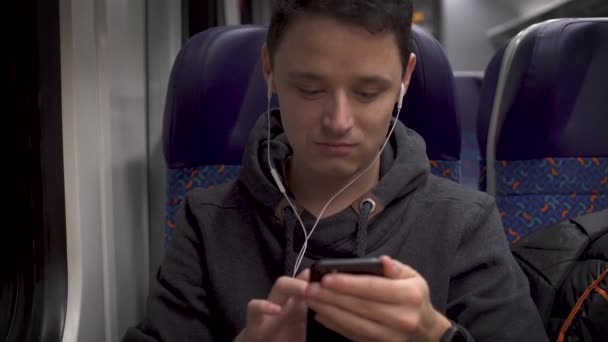 Genç adam trende çalışıyor, akıllı telefonuyla eğleniyor ve müzik sunuyor. — Stok video