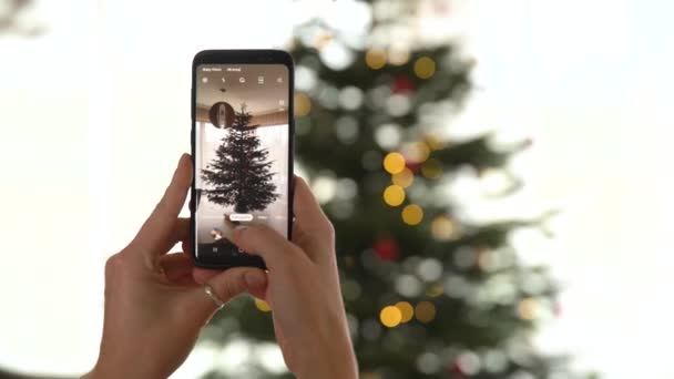 Séance photo avec téléphone intelligent sapin de Noël décoré et brillant dans différentes couleurs — Video