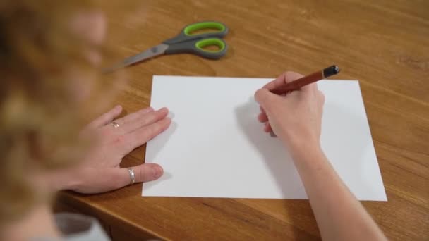 Młoda kobieta rysuje serce na białym papierze i tnie je nożyczkami. Produkcja prezentów z miłości — Wideo stockowe
