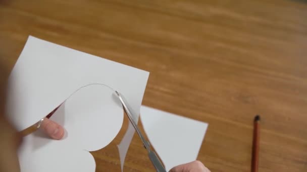 Una giovane donna disegna un cuore su una carta bianca e poi lo taglia con le forbici. Produzione di regali per amore — Video Stock