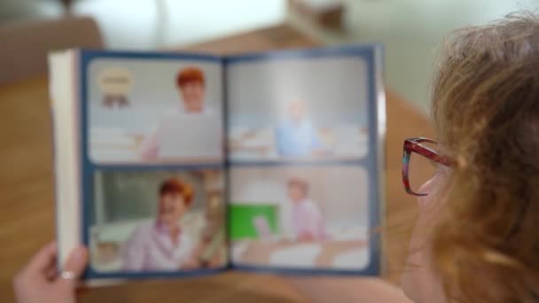 Een vrouw bladert door een album met foto 's van een middelbare school studio — Stockvideo