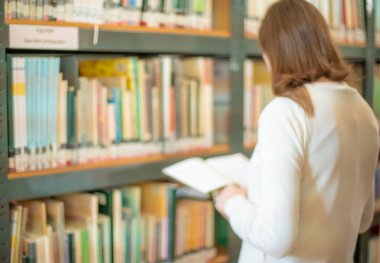 Kadın kütüphaneden bir kitap seçiyor ve okuyor.