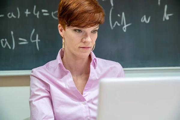 Ung lärare kollar läxor på sin bärbara dator i ett klassrum grundskola — Stockfoto