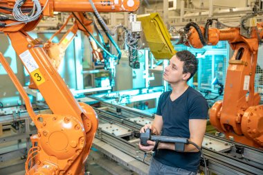 Mühendis kontrolleri fabrikadaki endüstriyel robotların uzaktan kumandasını kullanıyor. Otomatik kaynak ve yapıştırma otomasyon ve robotik kollar kullanarak