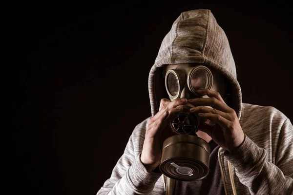 Homem coloca máscara de gás para proteger contra o gás. Retrato sobre fundo preto, coloração dramática — Fotografia de Stock
