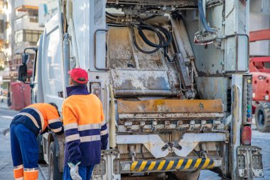 Büyük bir şehrin sokaklarında özel bir arabanın konteynırından atık topluyorlar.