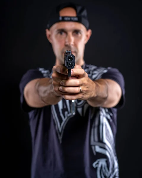 Homem apontando arma para objeto, retrato sobre fundo preto — Fotografia de Stock