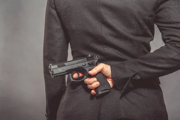 Pistole in der Hand hinter dem Rücken der Agenten versteckt. Porträt einer Frau mit Waffe auf grauem Hintergrund, Kopierraum — Stockfoto
