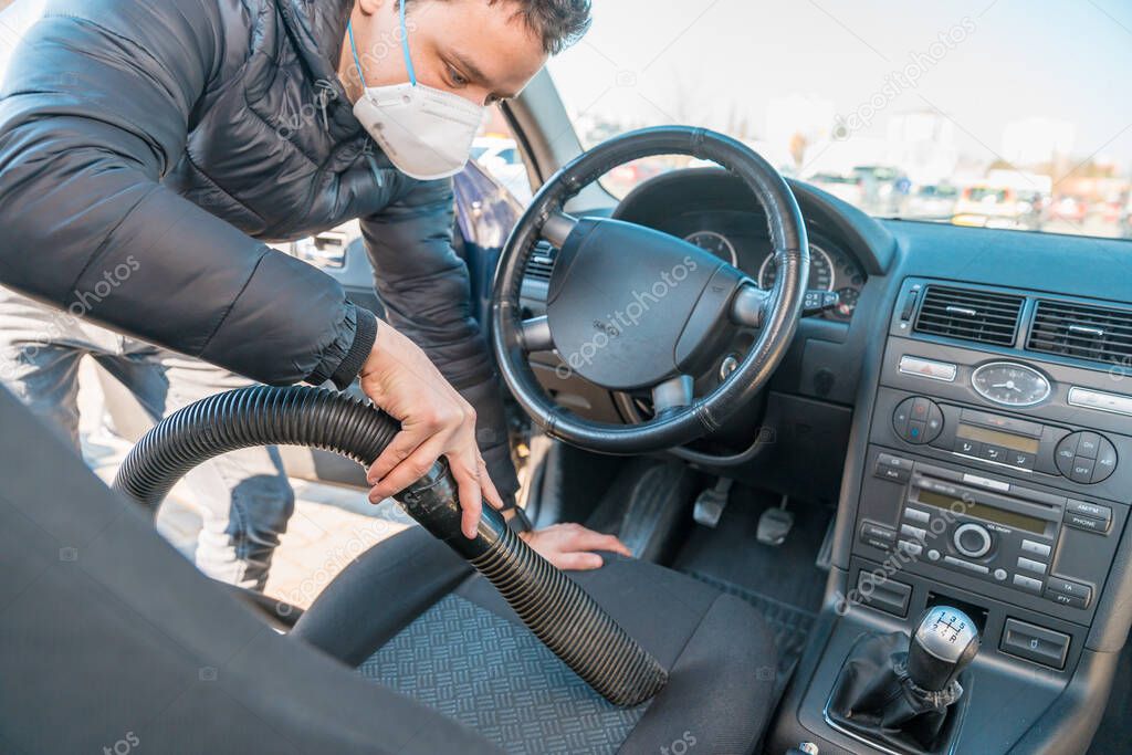 vacuuming the interior of a car with a respirator on the face during a coronavirus epidemic