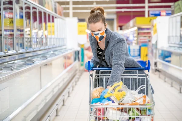 Mujer comprando comestibles en un supermercado durante una epidemia de coronavirus con una máscara médica en la cara — Foto de Stock