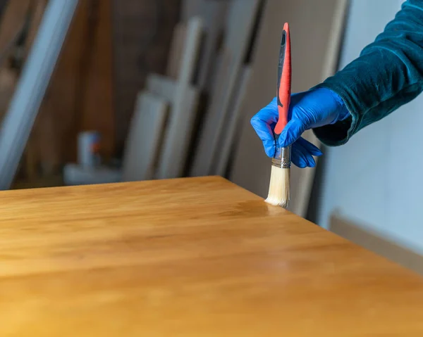 Revestimiento de superficie de madera con barniz protector. mano en guante de goma azul utiliza cepillo. Copiar espacio — Foto de Stock