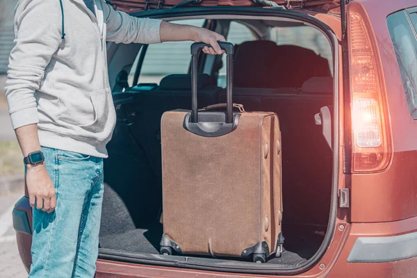 Un joven pone equipaje en el maletero de un coche — Foto de Stock