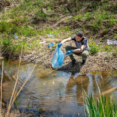 Nehir kıyısında bir gönüllü tarafından plastik atıkların temizlenmesi. Doğaya yardım etmek ve çevreyi korumak