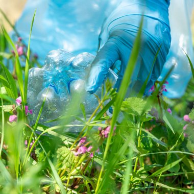 Doğada plastik atık toplayan lastik eldivenli bir adamın eline yakın plan.