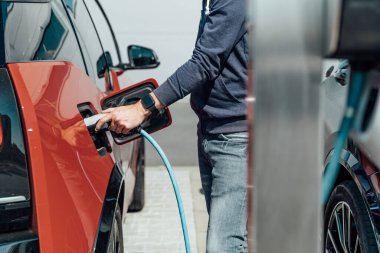 Adam şarj istasyonunda elektrikli arabayı şarj ediyor.