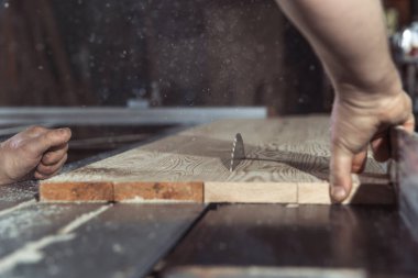 Bir adam doğramacıda dairesel testere ile odun kesiyor.