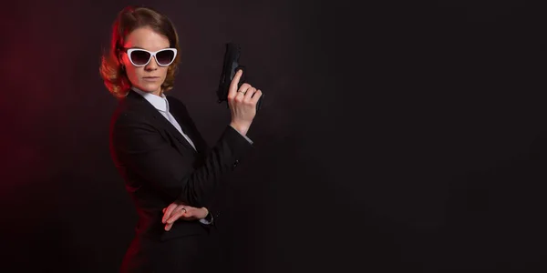 Una mujer de negocios con un arma en la mano. retrato sobre un fondo negro. banner con espacio de copia —  Fotos de Stock