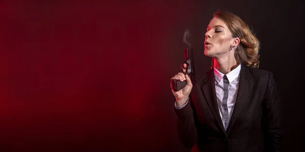 Soplando humo de un arma después de un disparo. portret de una mujer de negocios sobre un fondo oscuro. banner con espacio de copia —  Fotos de Stock