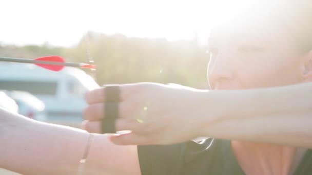 Femme concentrée tirant une flèche avec un arc lors d'une compétition de tir à l'arc en plein air. flash du soleil — Video