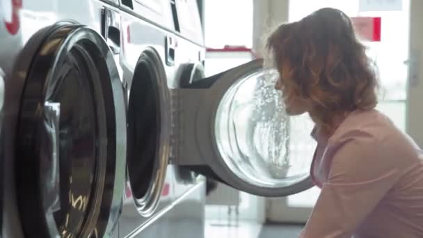 Витягування білизни з пральної машини в громадському пральні молодою жінкою — стокове відео