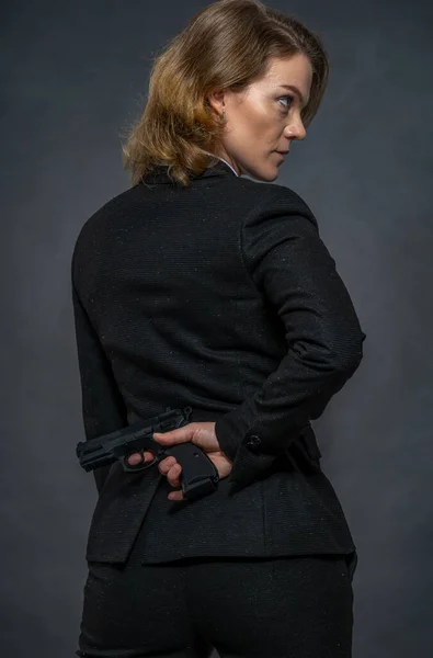 Gun in hand behind the back of a woman in a suit — Stock Photo, Image