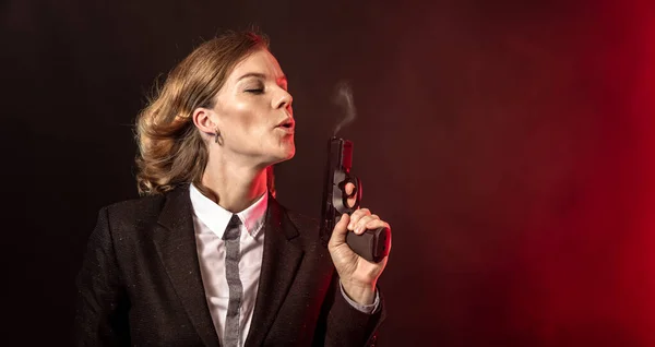 Soplando humo de un arma después de un disparo. portret de una mujer de negocios sobre un fondo oscuro. banner con espacio de copia —  Fotos de Stock